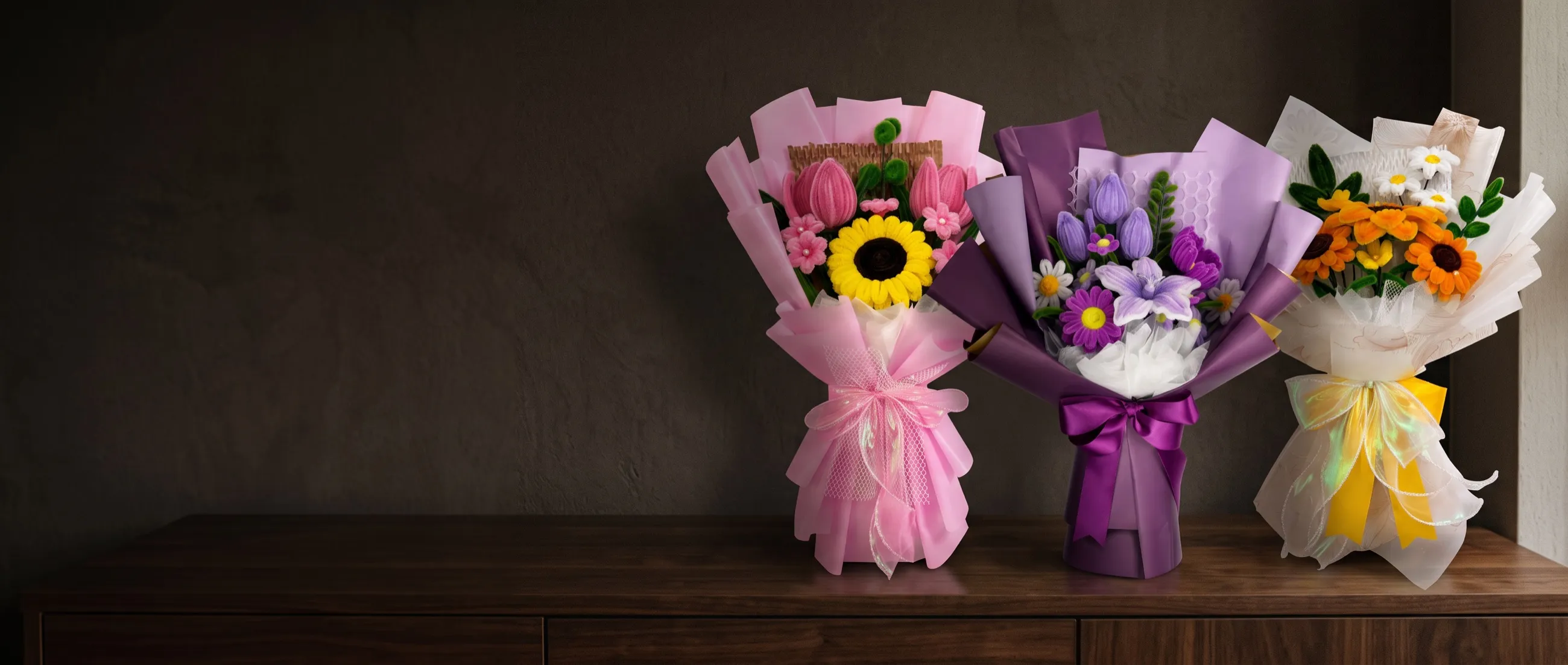 Tres ramos de Flor y Forma sobre un aparador de madera oscura: uno rosado con girasol, uno morado y uno blanco con girasoles naranjas